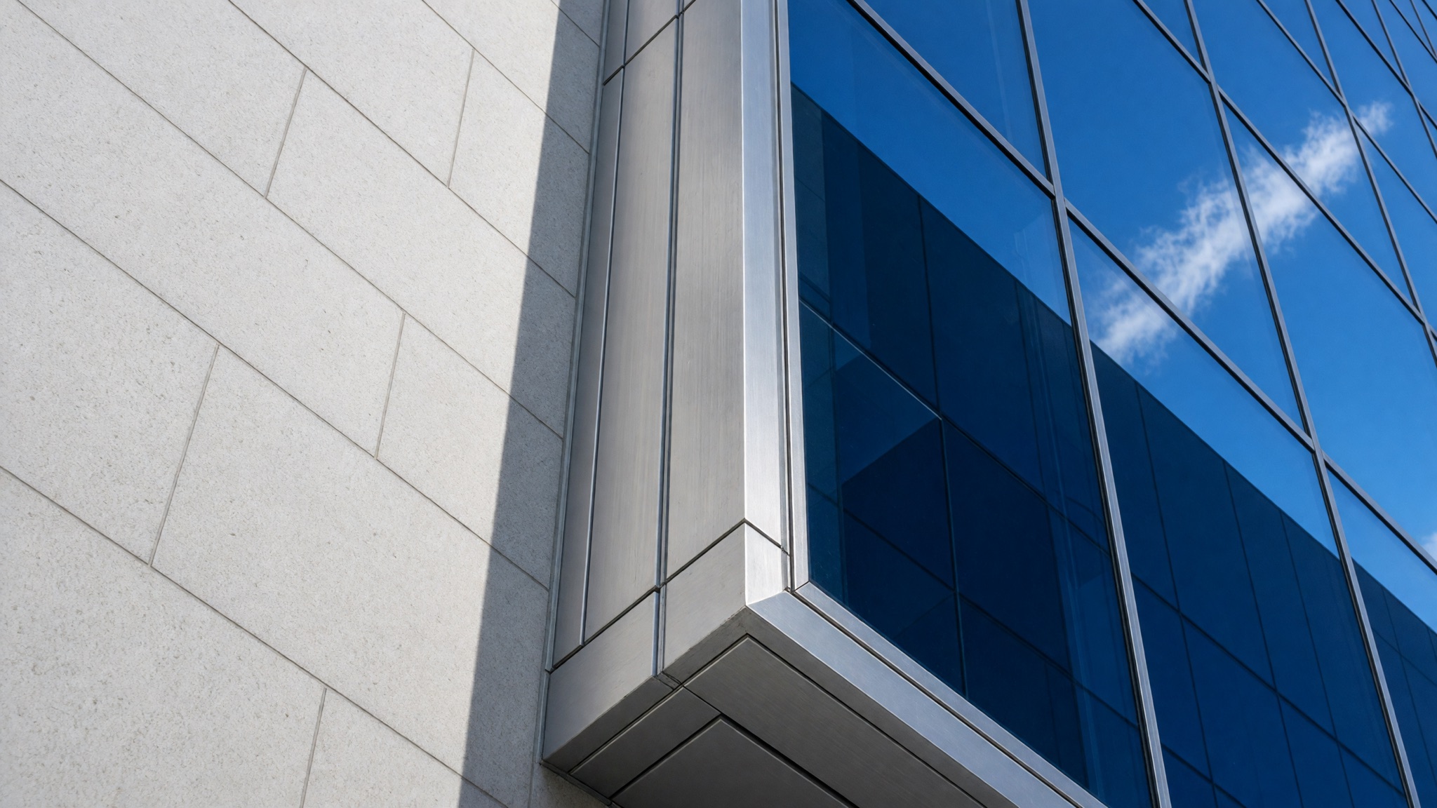 An upward view of a city corner, where pale stone and reflective glass meet a blue sky.